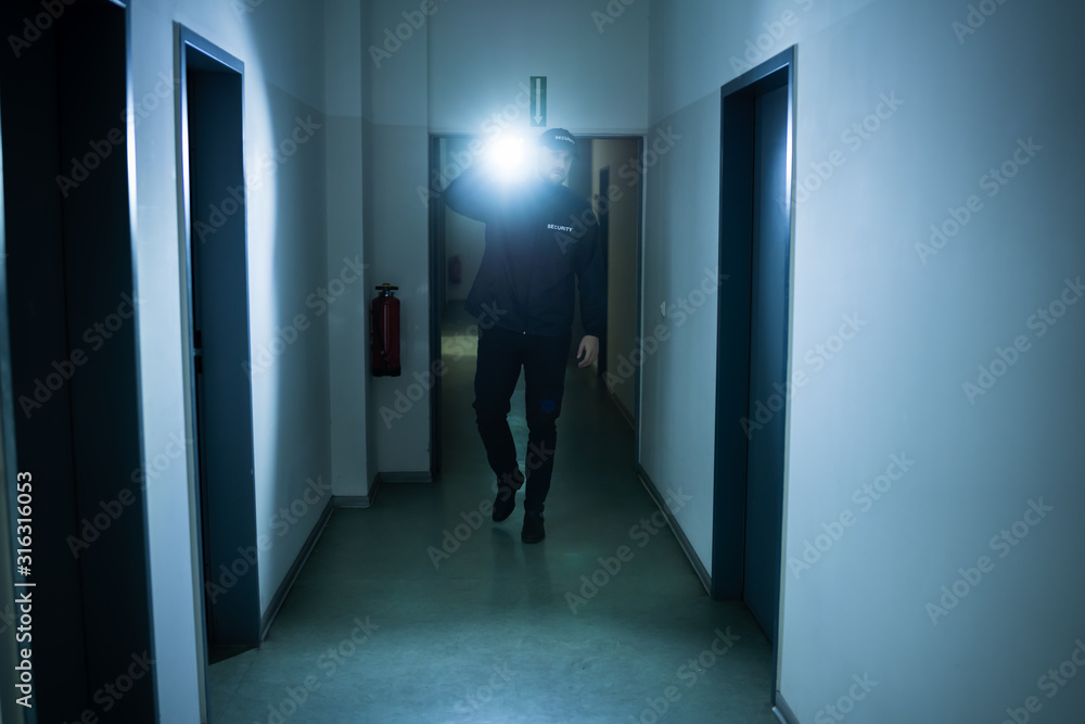 Fototapeta premium Security Guard With Flashlight In Building Corridor