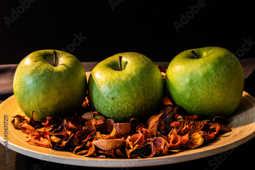 Group of green apples on plate with dried flowers