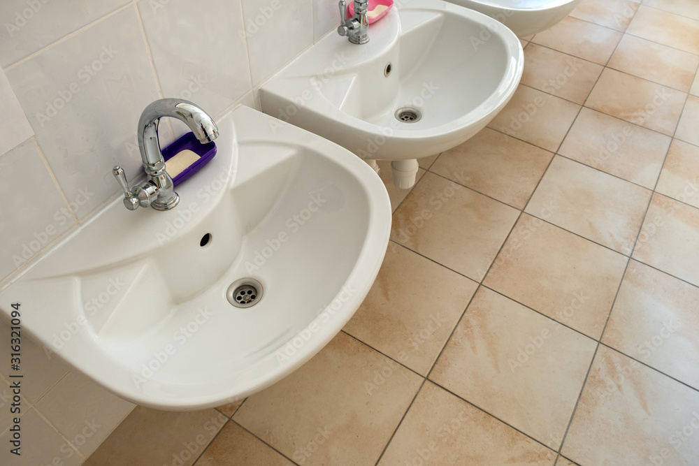 Fototapeta premium White ceramic washing basins with shiny stainless steel water tap.