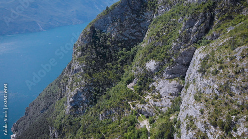 drone is flying along high mount near famous lake Garda, showing small building in cave of cliff in summer day