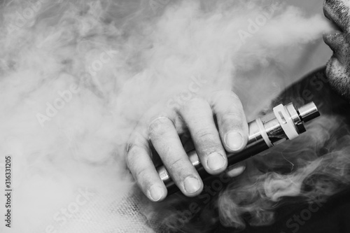 A man smokes an electronic cigarette, blowing a trickle of smoke. Harm to health, replacement of cigarettes, provoking cancer and other diseases. Close up.