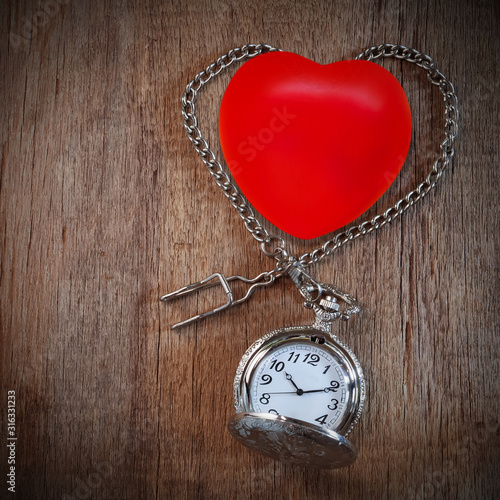 Red heart ball with vintage pocket watch on wood backround.