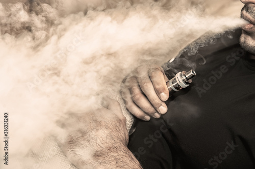 Canvas Print A man smokes an electronic cigarette, blowing a trickle of smoke