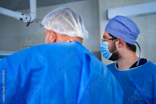 Group of doctors perform an operation to a patient. Surgeons in medical uniform and masks working in the operating room