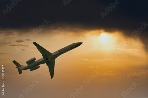 Airplane flying high in dark storm clouds and bright sun during sunset