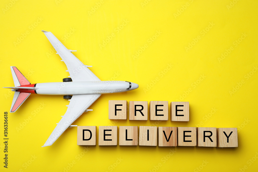 Flat lay composition of toy plane with words FREE DELIVERY on yellow background, space for text. Logistics and wholesale concept Flat lay composition of toy plane with words FREE DELIVERY on yellow background, space for text. Logistics and wholesale concept