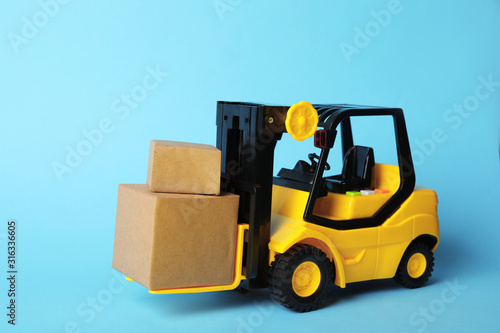Toy forklift with boxes on blue background. Logistics and wholesale concept