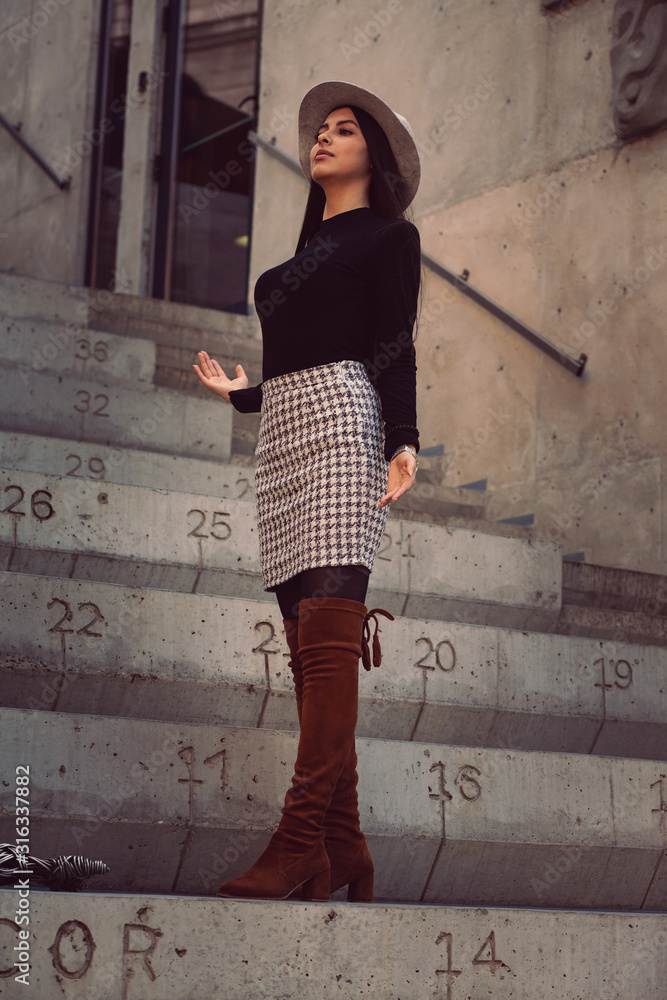 stylish girl in a hat with long hair posing on the steps of the building