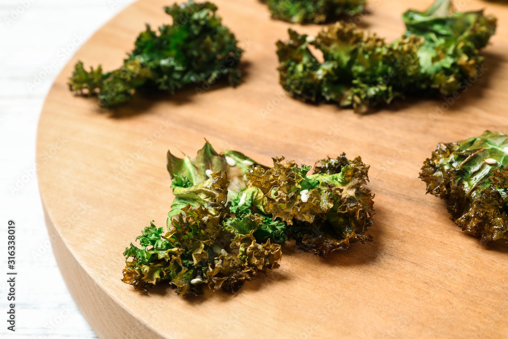 Tasty baked kale chips on wooden board, closeup Tasty baked kale chips on wooden board, closeup