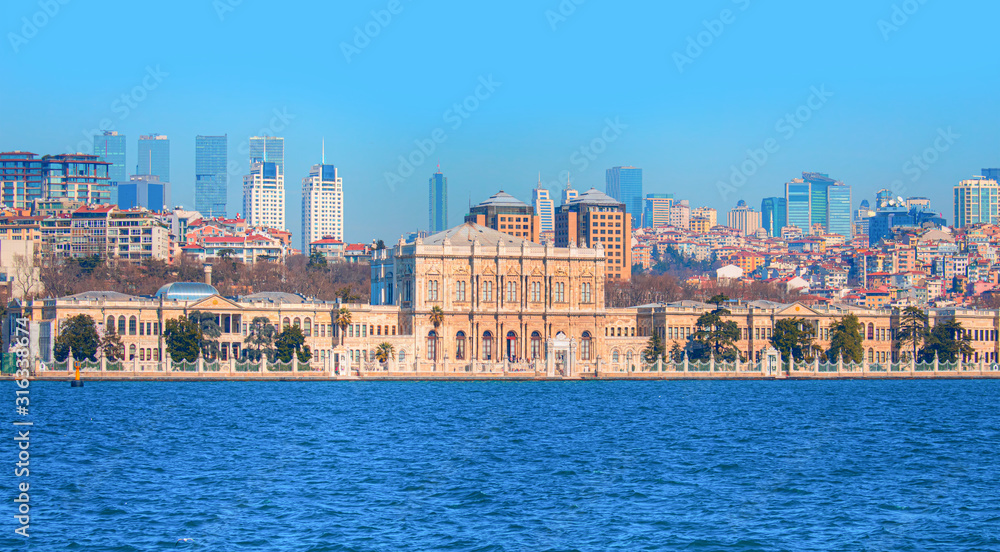Dolmabahce Palace (Dolmabahce Sarayi) seen from the Bosphorus - Dolmabahce palace against coastal cityscape with modern buildings under cloudy sky istanbul city
