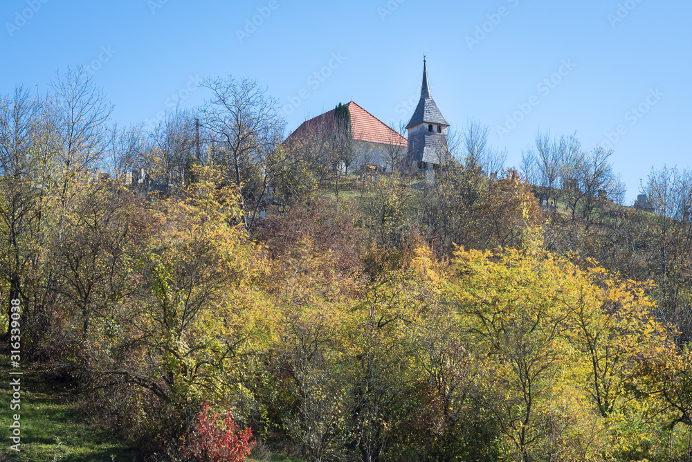 Old church on a hill in Transylvania, Romania. Trees with autumn leaf colors in the foreground.