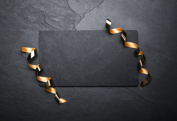 Slate board and serpentine streamers on black background, top view. Space for text