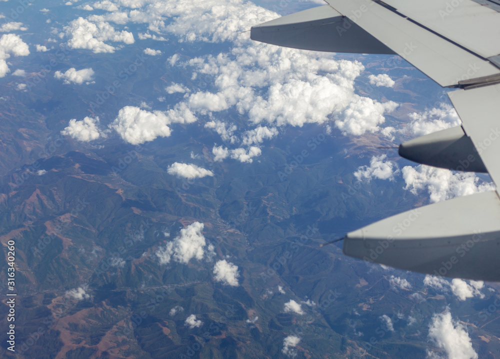 Closeup view of part of wing of flying above soft white fluffy clouds airplane as seen by passenger through porthole. Horizontal color photography. Closeup view of part of wing of flying above soft white fluffy clouds airplane as seen by passenger through porthole. Horizontal color photography.