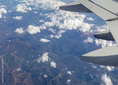 Closeup view of part of wing of flying above soft white fluffy clouds airplane as seen by passenger through porthole. Horizontal color photography.