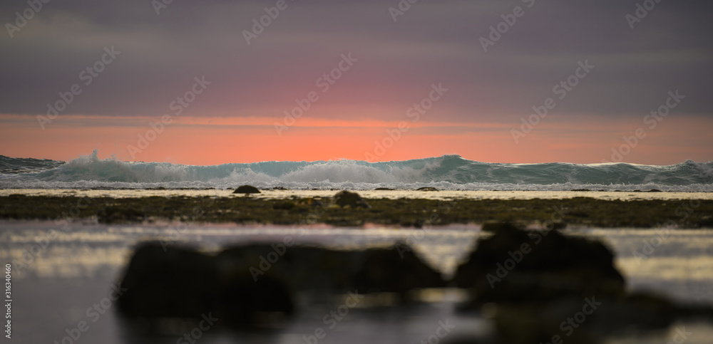 (Selective focus) Stunning view of waves crashing on a beautiful beach during a dramatic and romantic sunset. Lombok Island, West Nusa Tenggara, Indonesia.