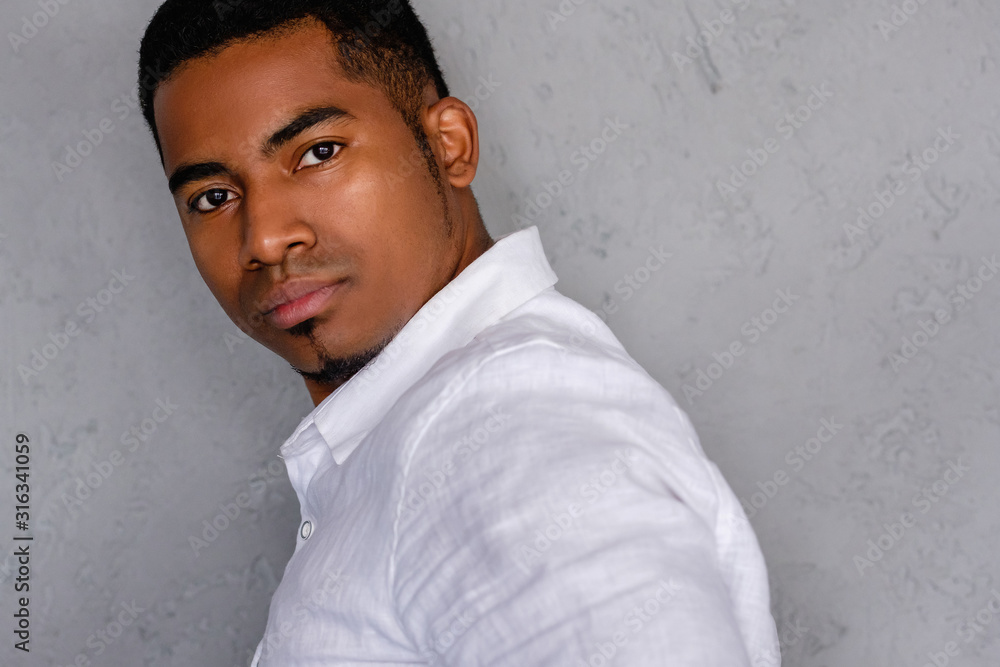 Close-up portrait of a serious handsome young african-american dressed in a white shirt posing on a gray bokeh background. Concept of confident successful young businessman. Advertising space Close-up portrait of a serious handsome young african-american dressed in a white shirt posing on a gray bokeh background. Concept of confident successful young businessman. Advertising space