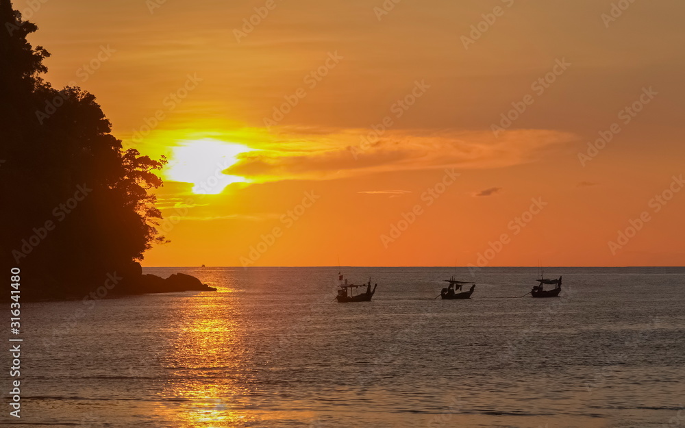sea view evening of fishing boats running in the sea with orange sun light in the sky background, sunset at Chong Khao Kad, Mu Ko Surin National Park, Phang Nga, southern of Thailand.