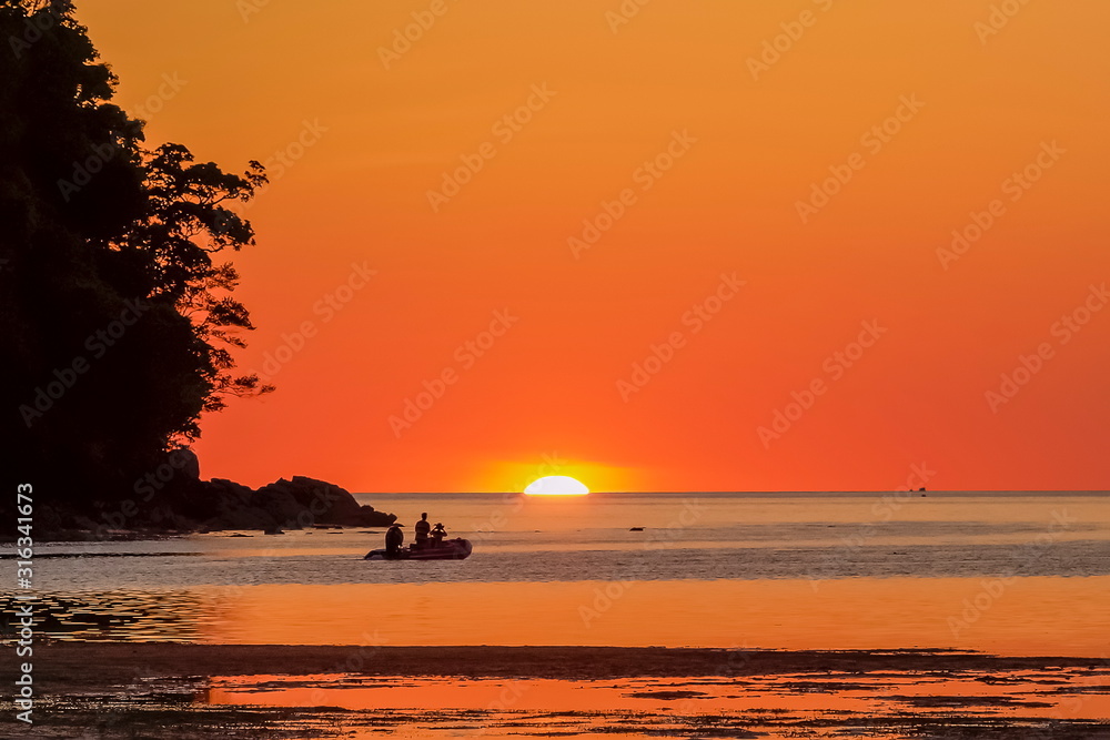 Sea view evening silhouette a rubber boat floating in the sea with sun dawn and red sky background, sunset at Khao Chong Kad, Surin island, Mu Ko Surin National Park, Phang Nga, southern of Thailand.