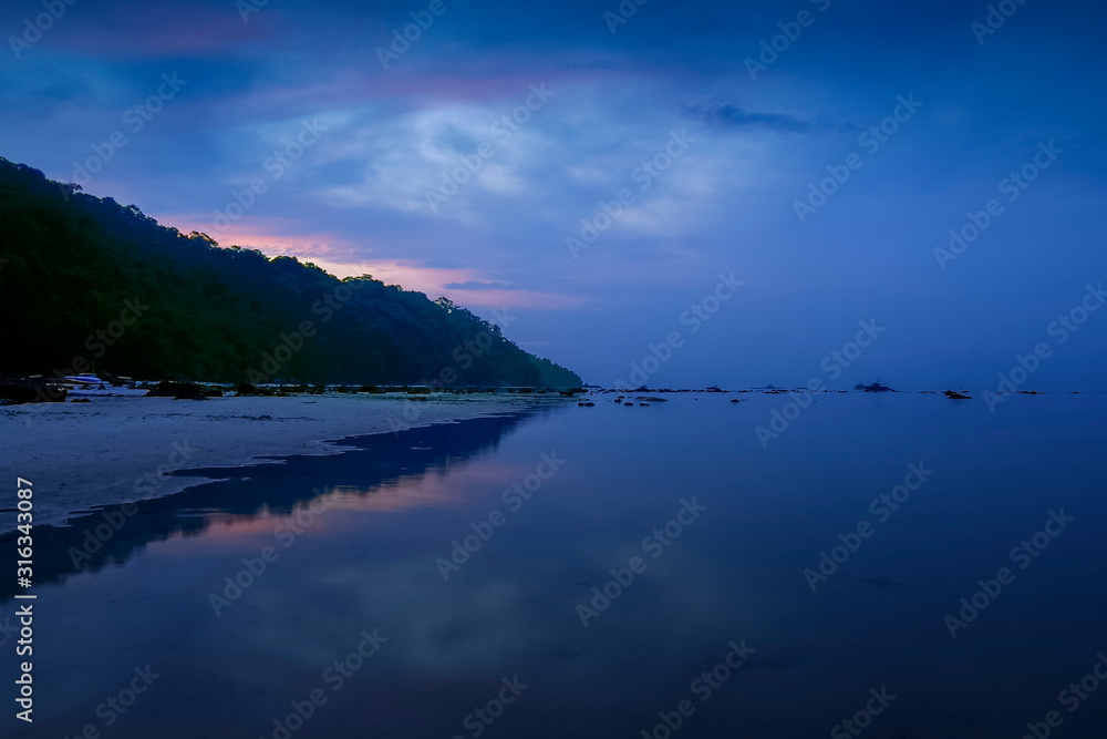 Sea view morning of white sand beach with mountain around with soft mist and red sun light in cloudy sky background, twilight at Khao Chong Kad, Surin island, Mu Ko Surin National Park, Thailand.