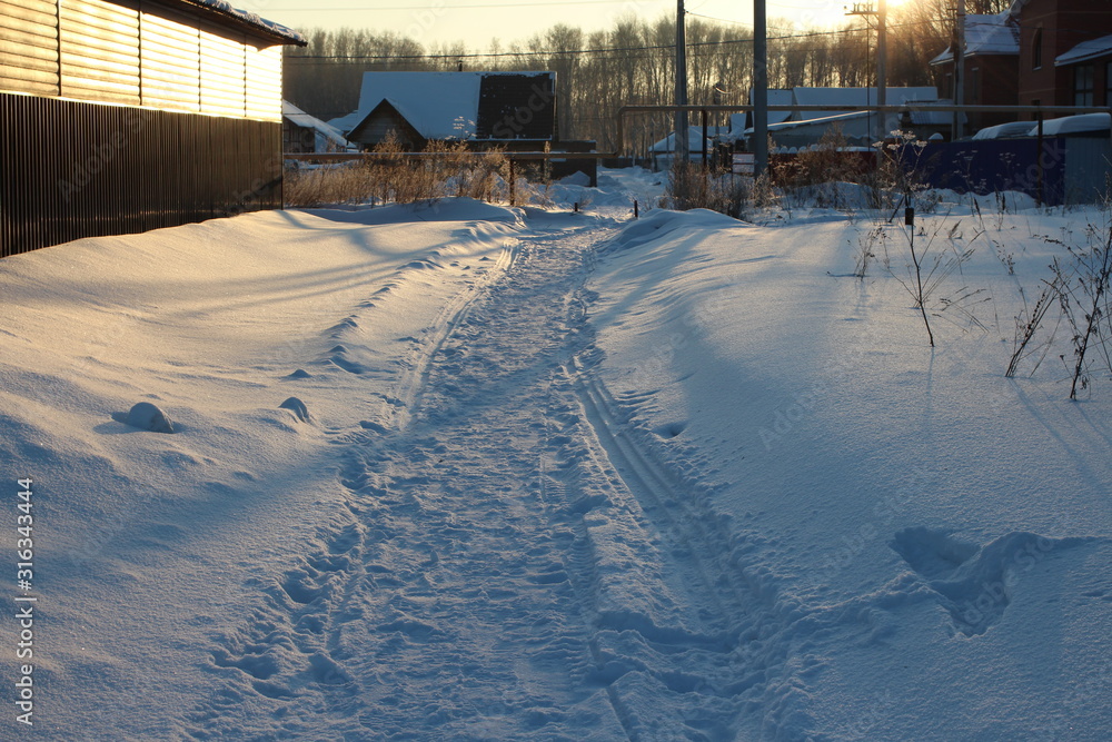a narrow well-trodden path for passing through the snow between the houses in the village in the evening