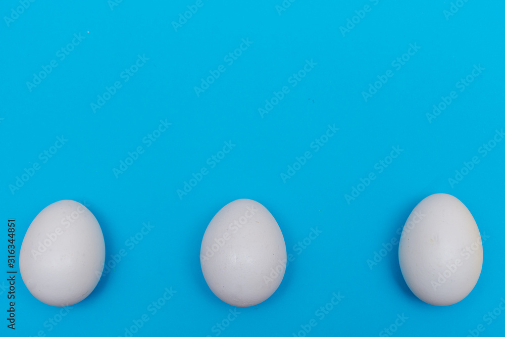 Three Easter holiday flat lay with white egg on a solid bright blue vibrant background with copy space on top. Three Easter holiday flat lay with white egg on a solid bright blue vibrant background with copy space on top.
