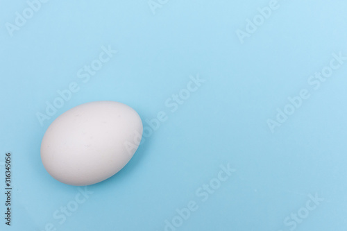 Easter holiday flat lay with white egg on a solid light blue pastel background with copy space.