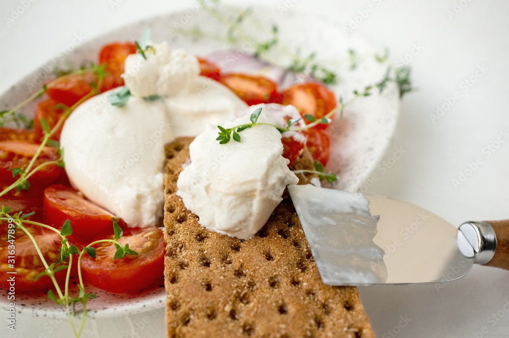 Sliced fresh Italian burrata cheese with tomato slices on bread on a white background. Close up. Selective focus Sliced fresh Italian burrata cheese with tomato slices on bread on a white background. Close up. Selective focus