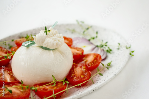 Fresh Italian burrata cheese with tomato slices on a light plate on a white background. Close up. Healthy Italian food. Selective focus