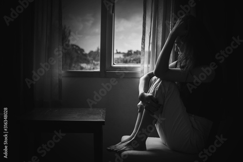 depress woman sitting on chair in room near window in white tone, sadness and depress concept