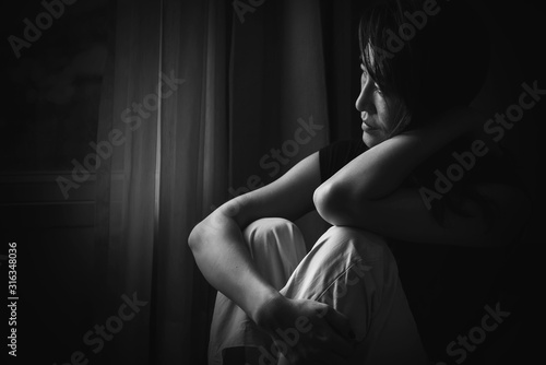 depress woman sitting on chair in room near window in white tone, sadness and depress concept
