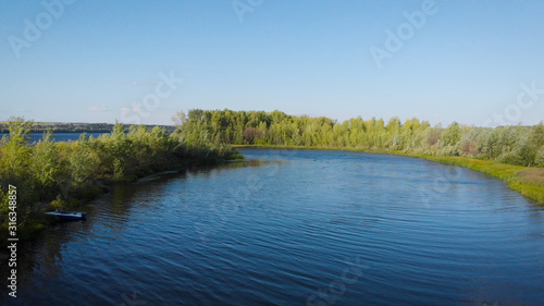 aerial view of calm small river and trees on shores in sunny weather in summer, camera is flying along coasts