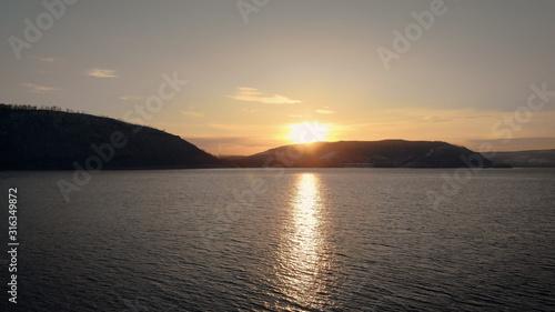 It's an aerial view. Sunset over the mountains. The river or lake is covered with people, freezes at the shore. Low flyover over water © kustvideo