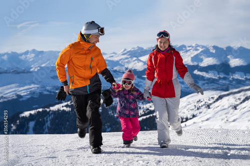Mother And Father Running On Snowy Slope With Their Daughter