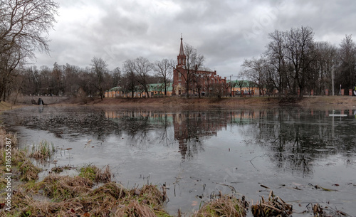 Ancient Lutheran church on the shore of a frozen pond, winter without snow, cloudy weather