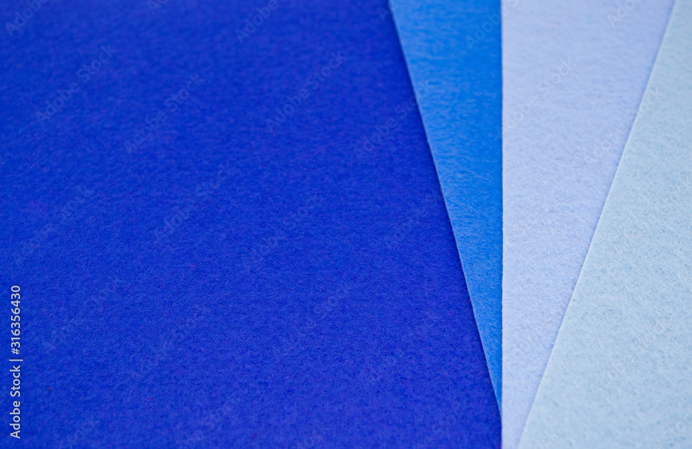 Close up of four pieces of felt of different shades of blue from dark to very light. Blue spectrum. Color of the year 2020. Copy space. On the left, on a dark blue background - a place for text Close up of four pieces of felt of different shades of blue from dark to very light. Blue spectrum. Color of the year 2020. Copy space. On the left, on a dark blue background - a place for text