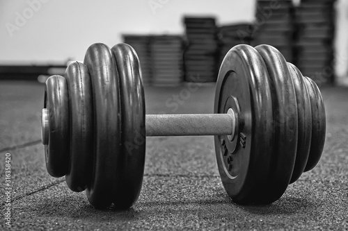 Fototapeta Naklejka Na Ścianę i Meble -  Heavy dumbbell on floor of the gym. Fitness concept. Black and white image