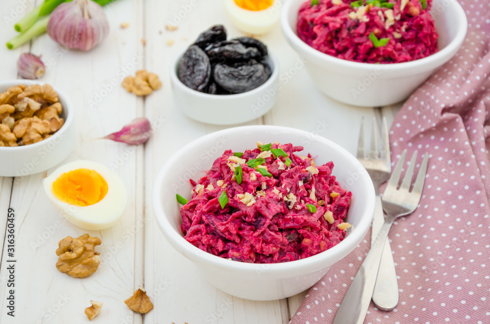 Salad of boiled beet. Beetroot salad with prunes, walnuts, eggs and sour cream in a bowl on white background. Healthy food. Horizontal orientation. Salad of boiled beet. Beetroot salad with prunes, walnuts, eggs and sour cream in a bowl on white background. Healthy food. Horizontal orientation.