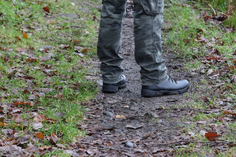 A photograph of a man's legs, standing on a forest woodland path, wearing camouflage trousers and black hiking boots. Outdoors, hiking, nature concept. A photograph of a man's legs, standing on a forest woodland path, wearing camouflage trousers and black hiking boots. Outdoors, hiking, nature concept.