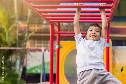 Soft​ focus.​ Kid exercise for health and sport concept. Happy Asian student​ child boy playing and hanging from a steel bar at the playground. 5 years old.