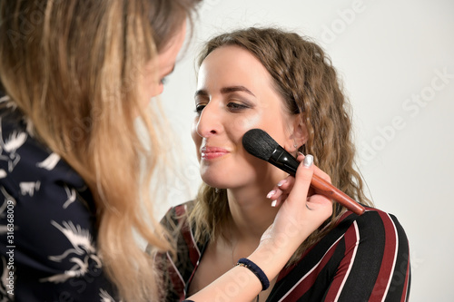 Applying cosmetics. Close-up portrait of a makeup artist doing makeup of a female model in a studio.