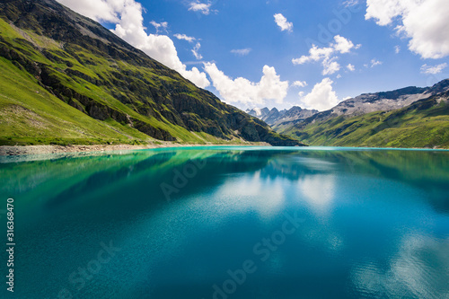 Fototapeta Naklejka Na Ścianę i Meble -  Mountains reflect in the clear blue water of the mountain lake Lac de Moiry in the Pennine Alps on a summer day with a nice blue sky and some white clouds. Grimentz, Valais, Switzerland