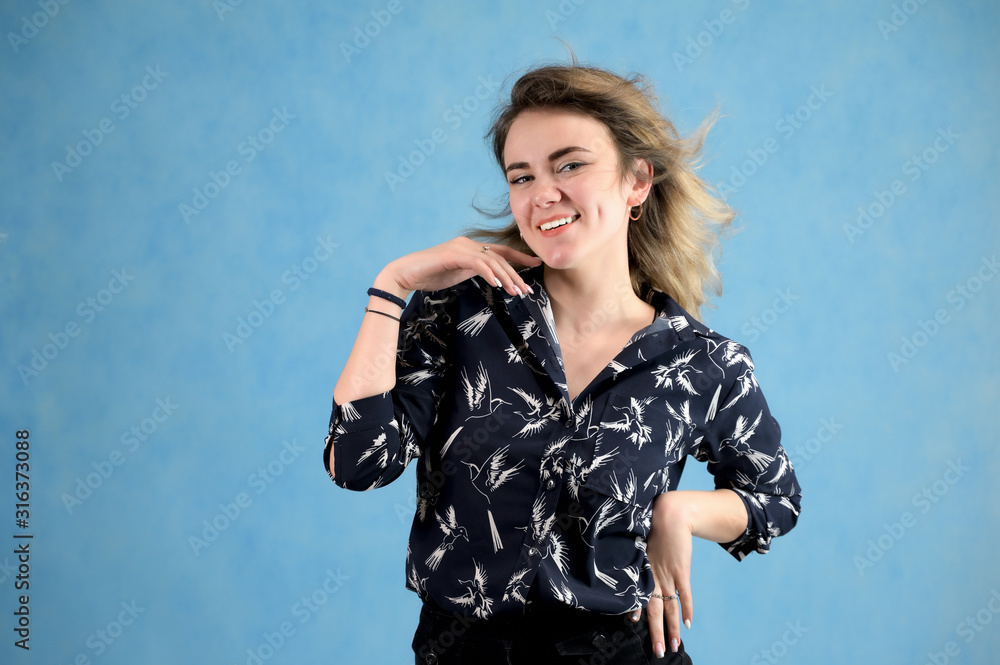 Concept woman in a dark blouse smiling talking. Portrait of a model girl with excellent makeup with curly hair and good teeth in the studio on a blue background. Concept woman in a dark blouse smiling talking. Portrait of a model girl with excellent makeup with curly hair and good teeth in the studio on a blue background.