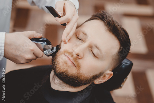 Barber shearing beard to man in barbershop framing hairline. electric razor, vintage tinted brown