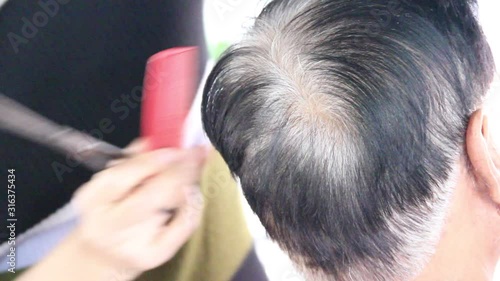 Hairdresser cutting client's hair in salon with scissors and comb