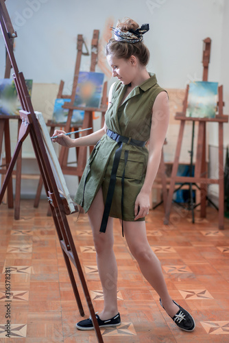 Full lenght portrait of a woman artist painting in the art studio.