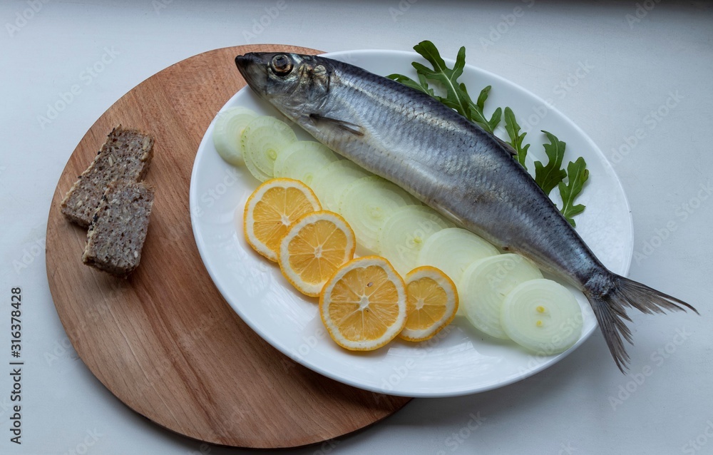 Salted fish - herring with onions, buckwheat bread and herbs, on a wooden board and white background. With crumpled craft paper. Yummy. Salted fish - herring with onions, buckwheat bread and herbs, on a wooden board and white background. With crumpled craft paper. Yummy.