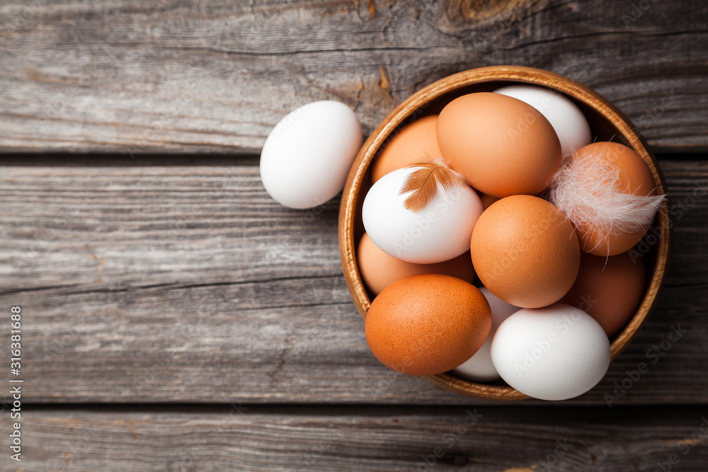 Fresh white and brown chicken eggs in a wooden bowl. Raw eggs on wooden background