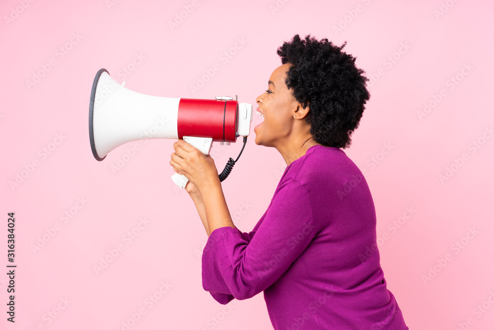 African american woman over isolated pink background shouting through a megaphone African american woman over isolated pink background shouting through a megaphone