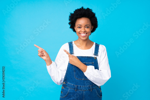 African american woman with overalls over isolated blue background pointing finger to the side photo