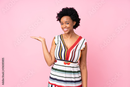 African american woman over isolated pink background holding copyspace imaginary on the palm to insert an ad